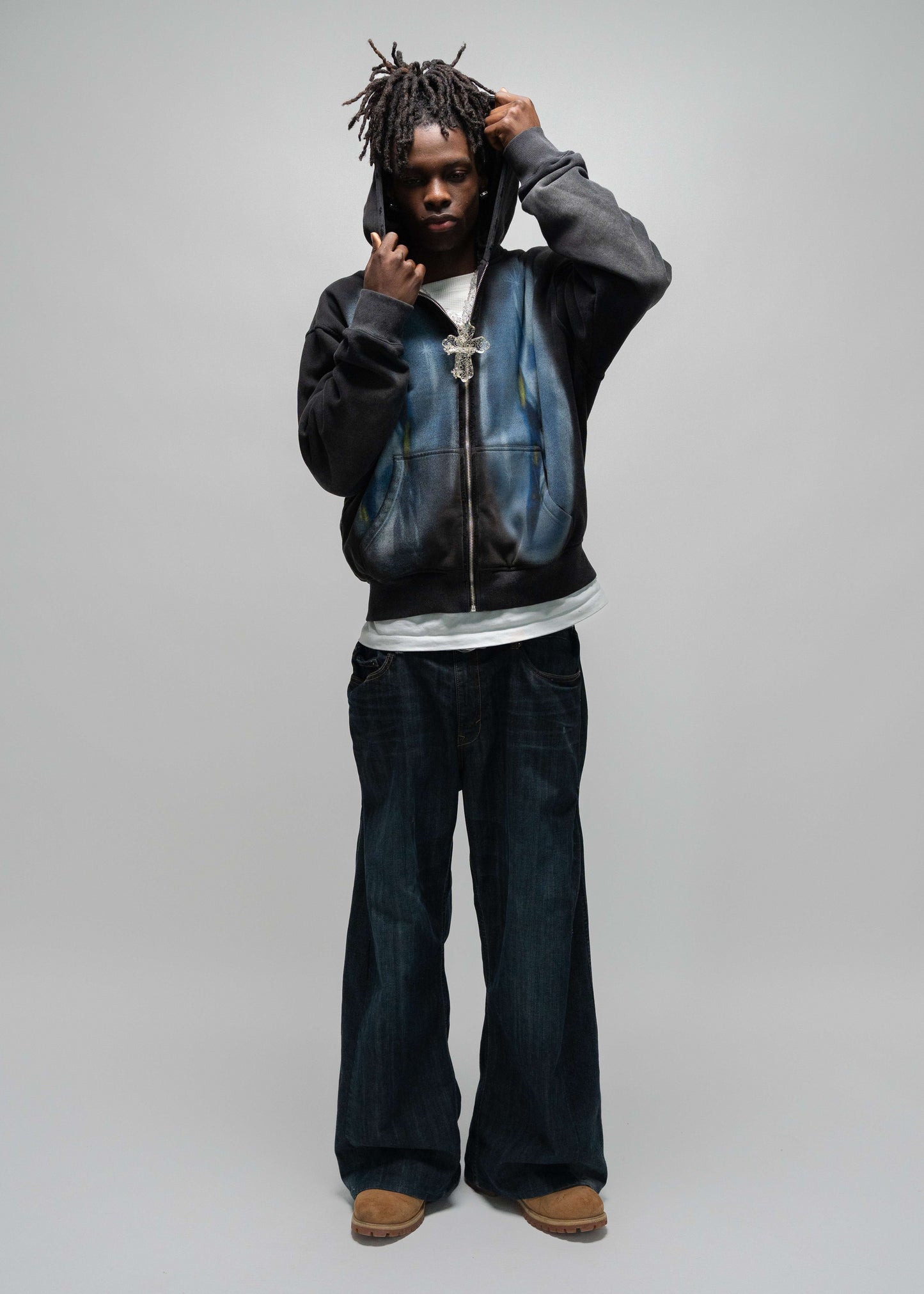 another full body pose while the model is wearing the dogfight zip up by j3t. he has his right hand above his ear while his left hand is just below his chin. His hand are holding up the hood. jet hoodie