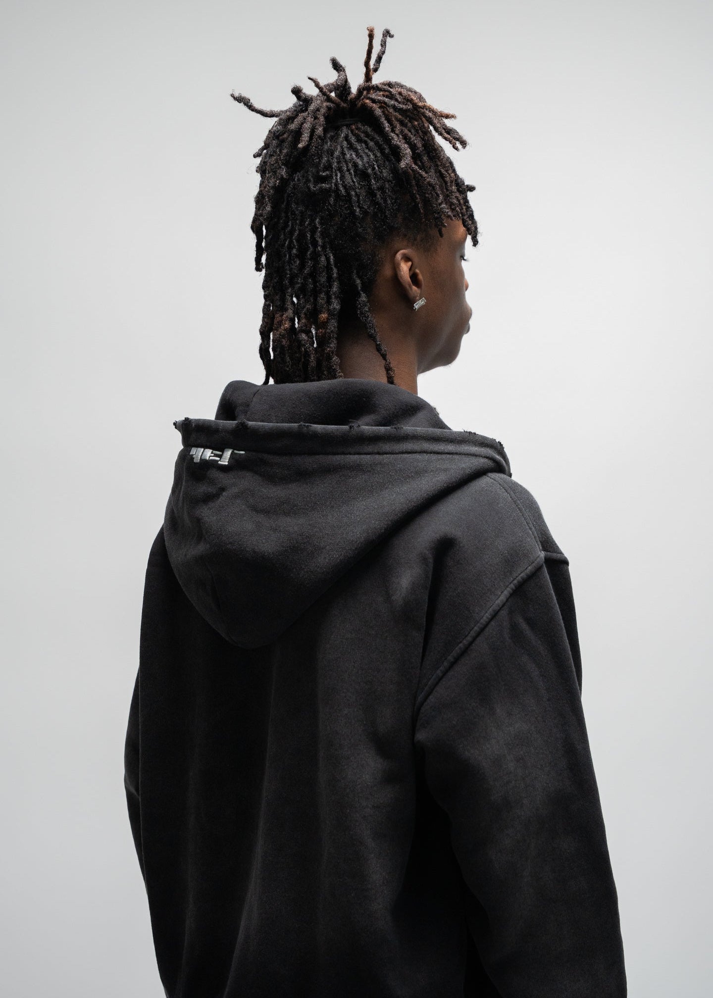 back view 45 degree angle of the model wearing the dogfight zip up by j3t. It is only showing his upper body. This shot focuses on the embroidery and distressing on the hood. J3T APPAREL