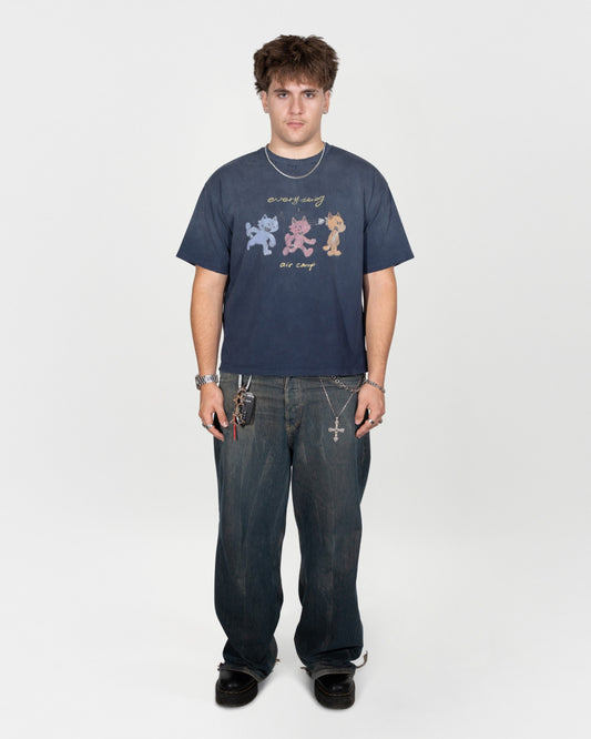 Full body 45 degree angle shot. The model is facing directly at the camera. serious facial expression with hands down by his hips. He is wearing the air camp tee by j3t with dark greyish blue jeans and black shoes.