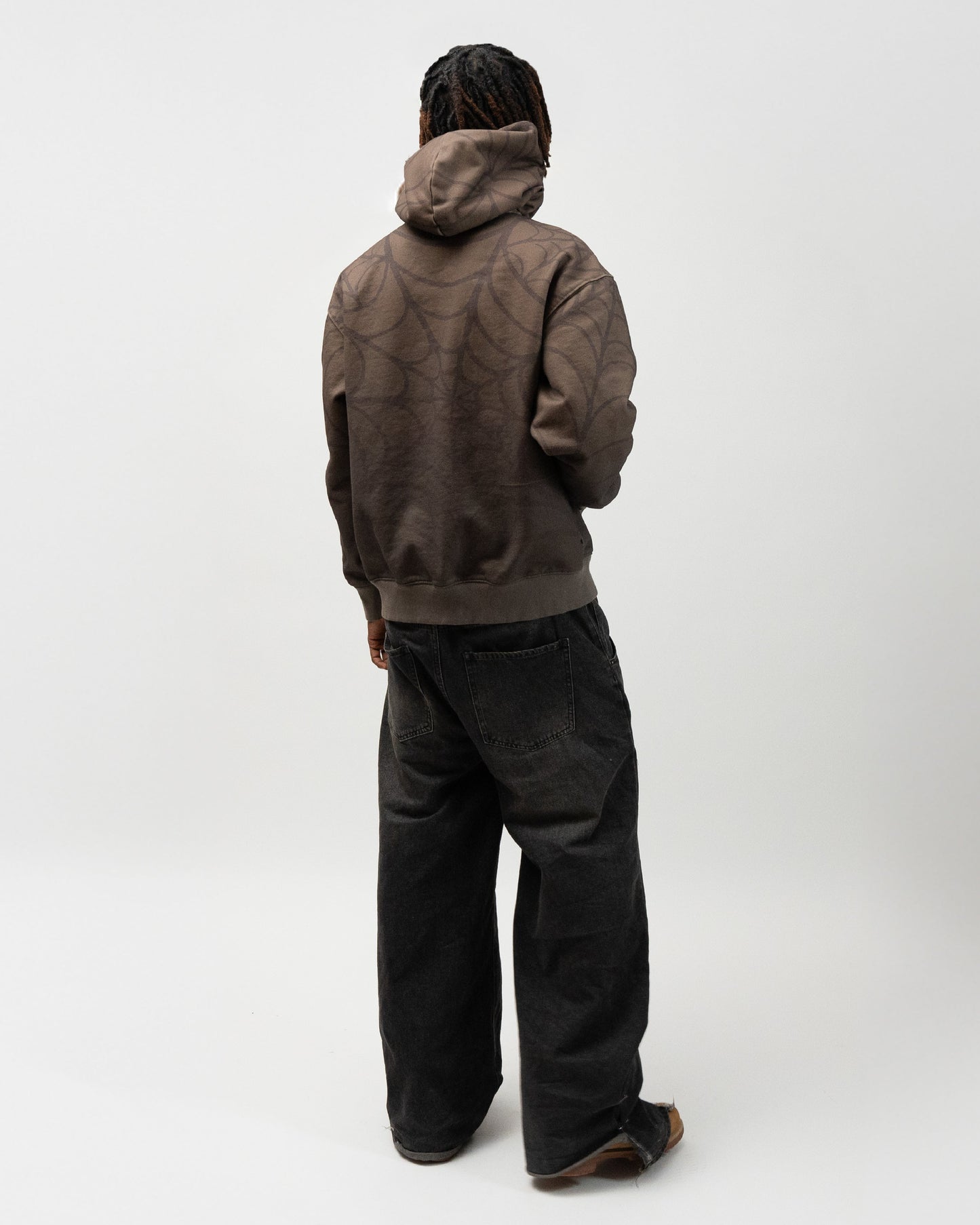 Full body angle of the model posing. He is turned away from the camera and facing the wall. he does not have the hood on and has his right hand in the pocket of the hoodie. J3T hoodie