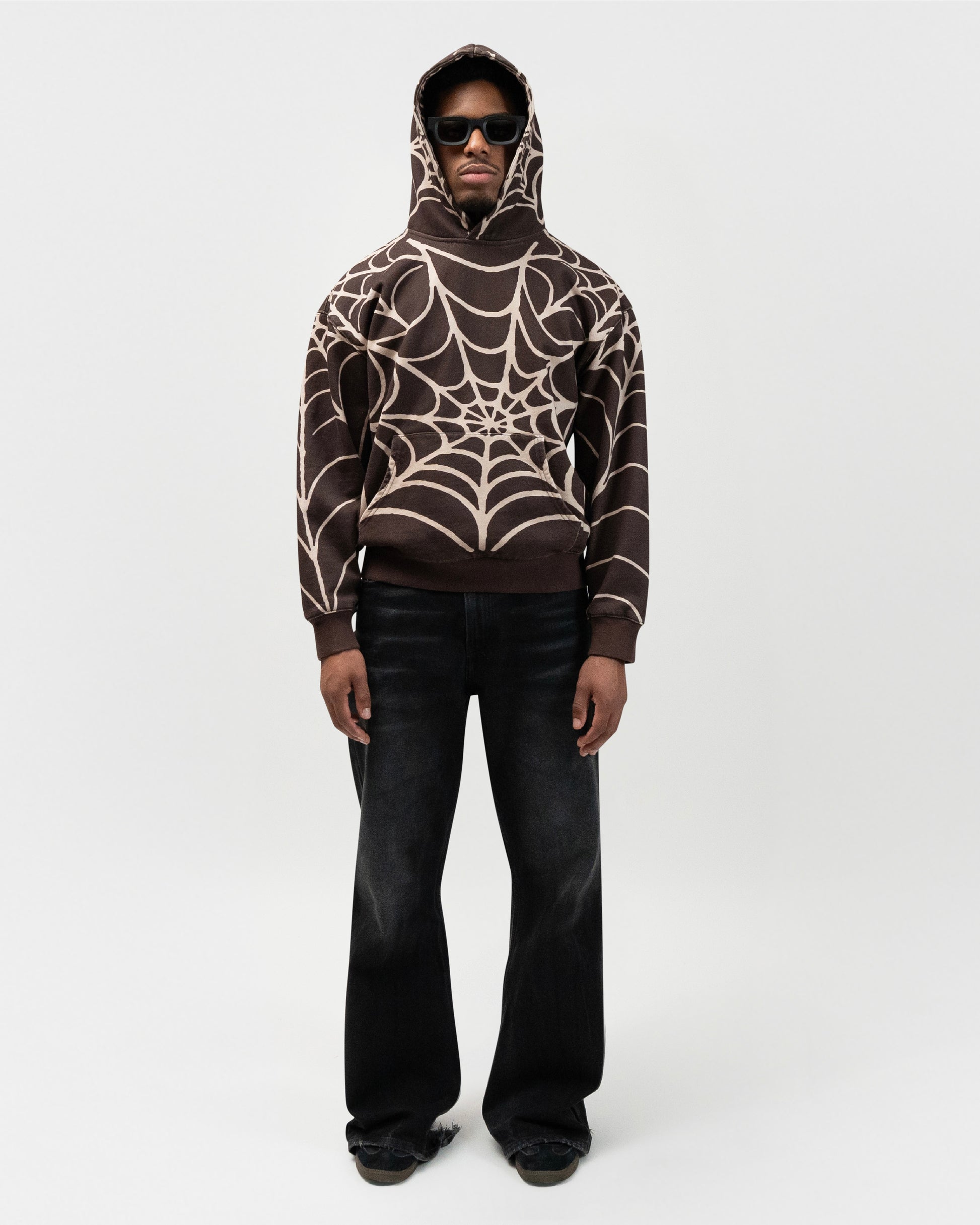 Full body angle of male model wearing the brown spider hoodie by j3t. His right hand is in the pocket of his pants. j3t apparel