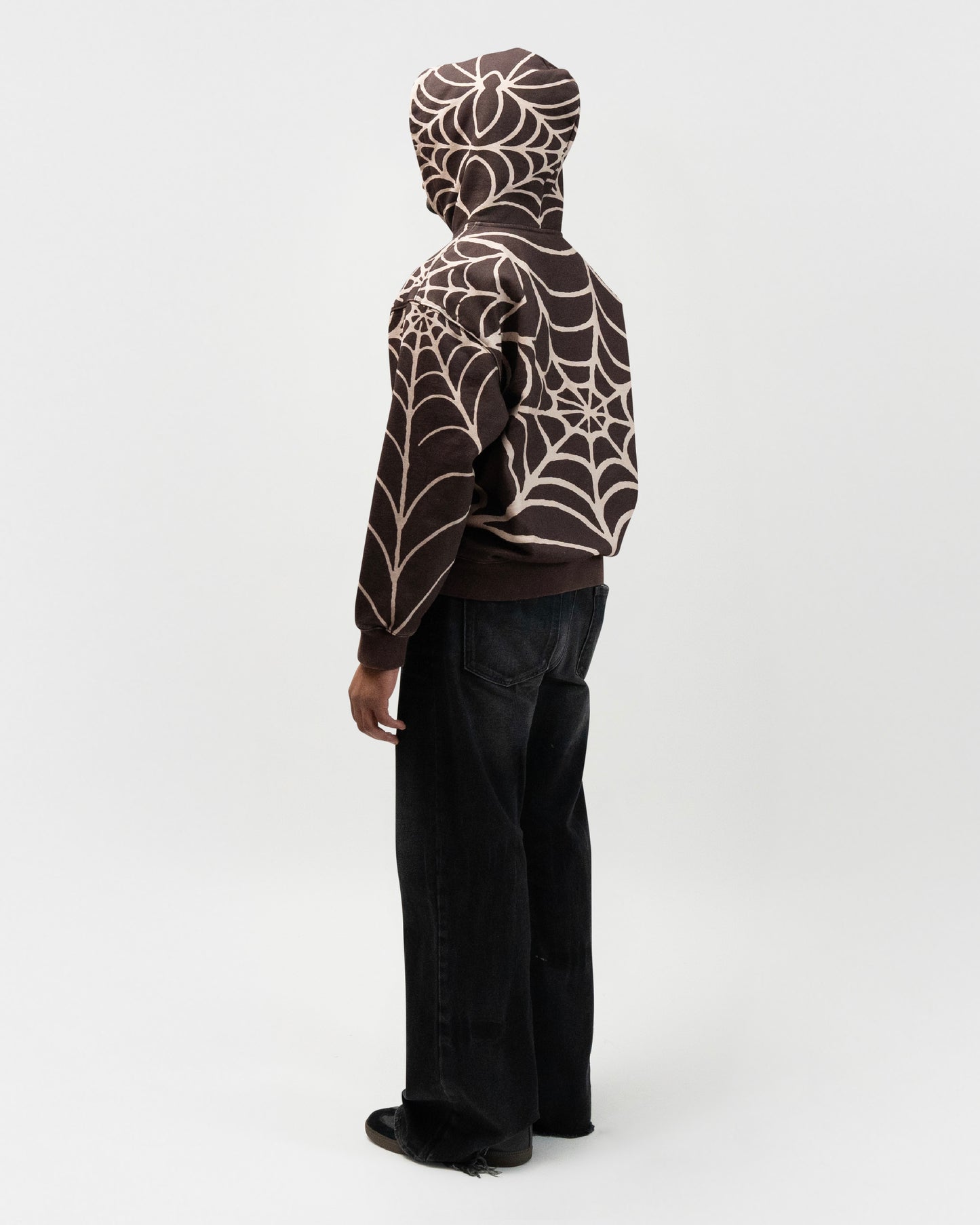 Full body back angle of the model wearing the brown spider hoodie by j3t. He is standing at a 45 degree angle. everythingj3t