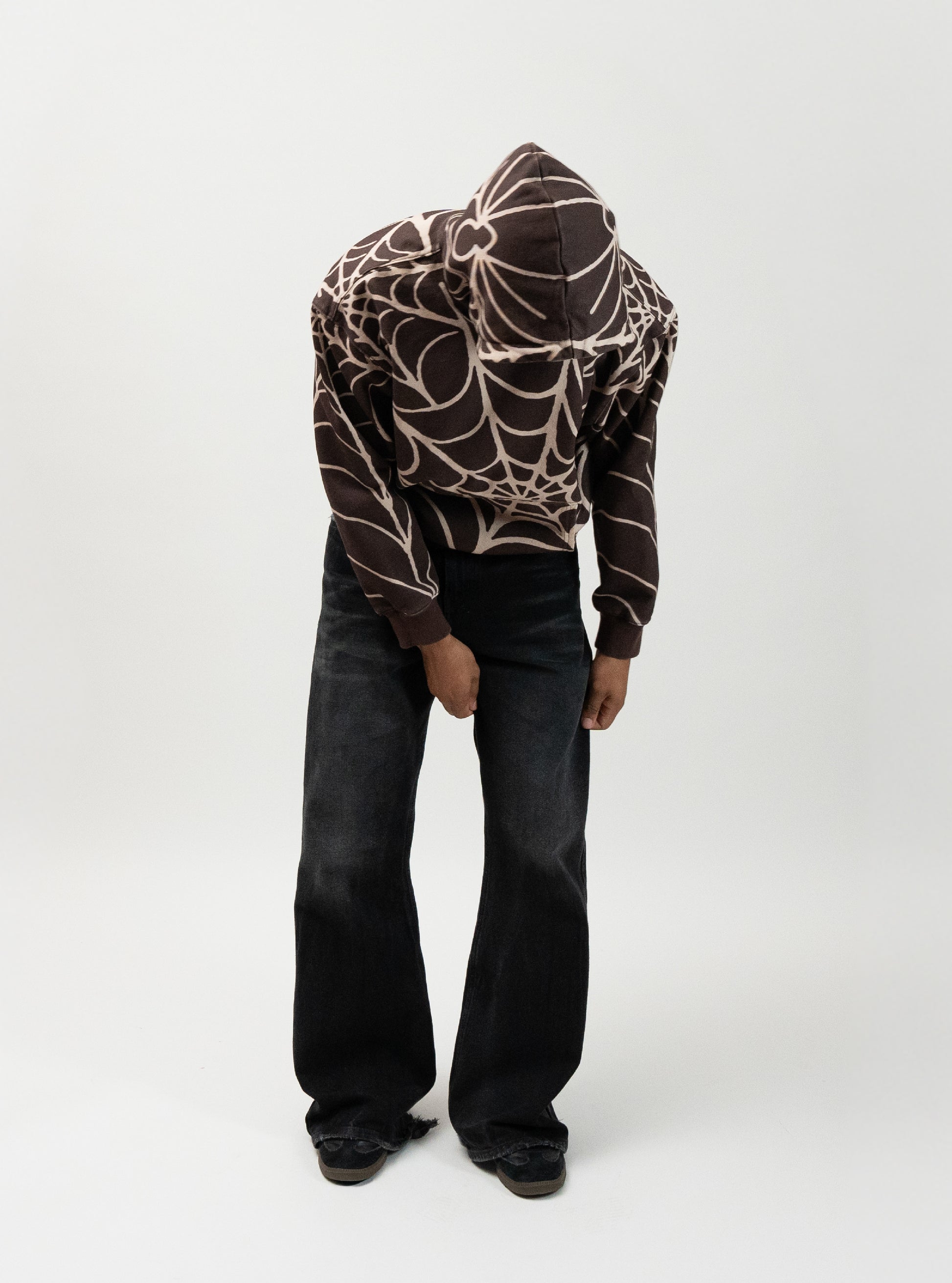 male model posing while wearing the brown spider hoodie. he is performing the motion of fixing his pants. spider hoodie by j3t