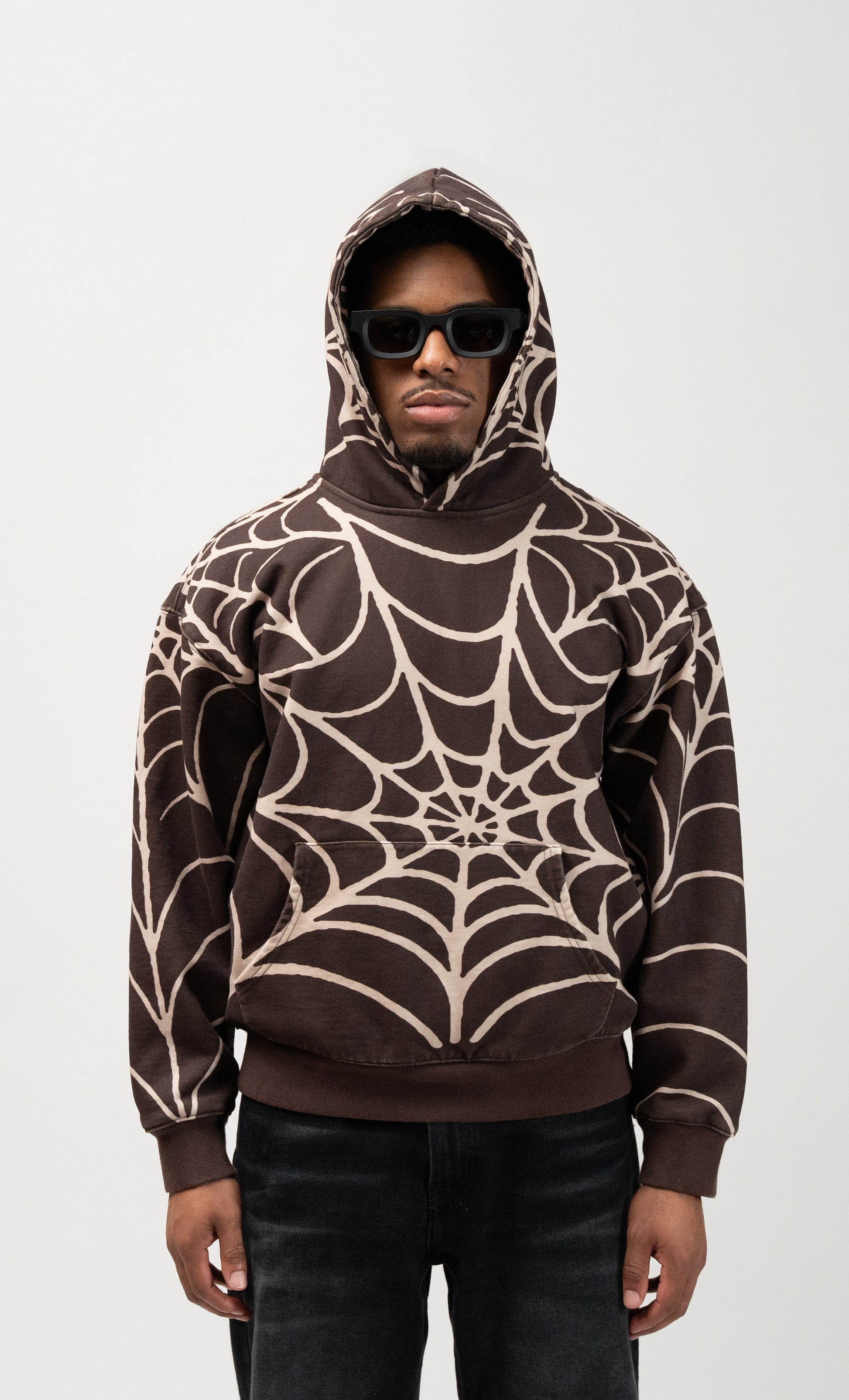 medium shot of a male model wearing the spider hoodie with allover print. from right above his knees and up. brown j3t spider hoodie