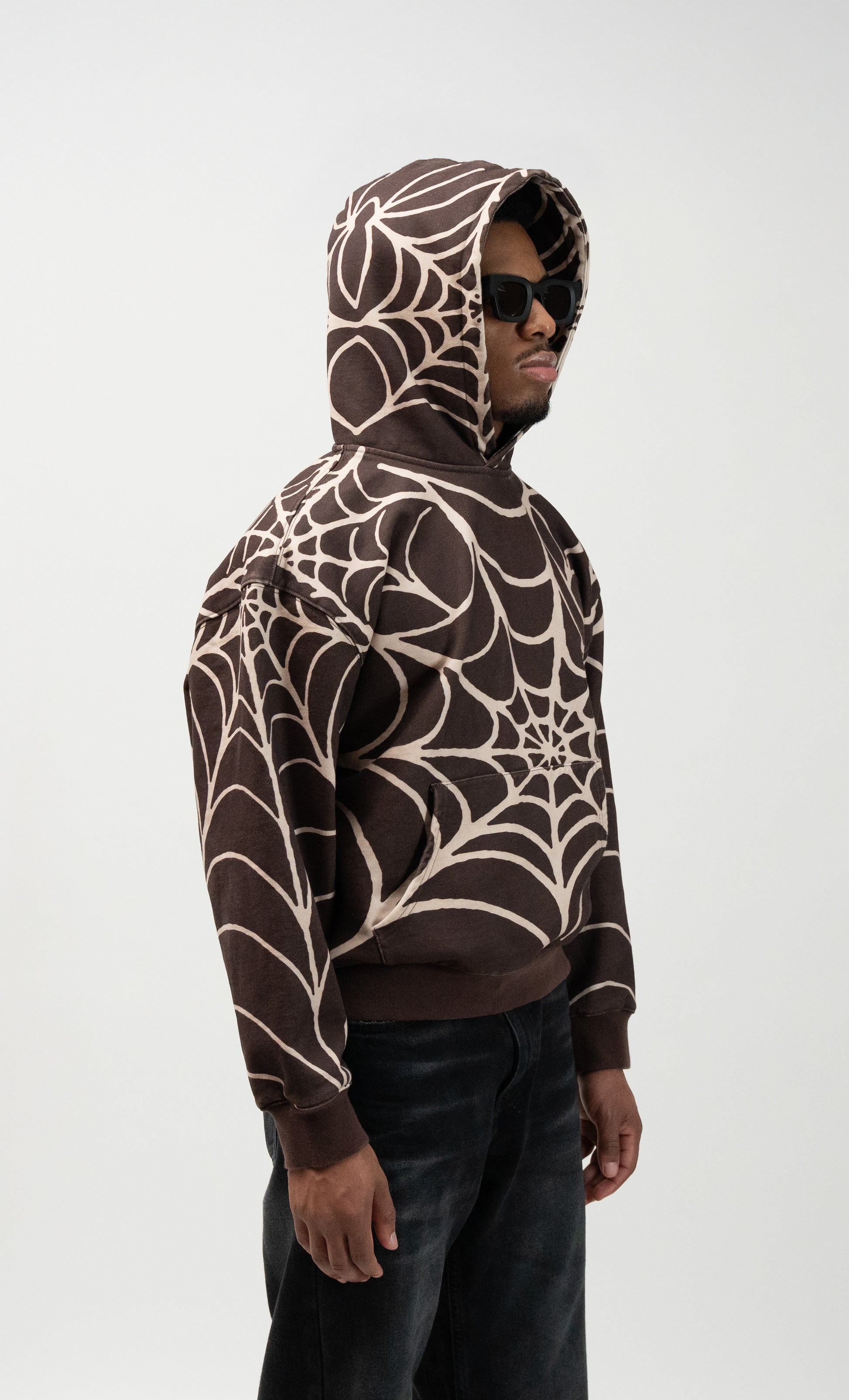 45 degree angle, medium shot of male model wearing the j3t spider hoodie. he has the hood on and sunglasses as well. j3t