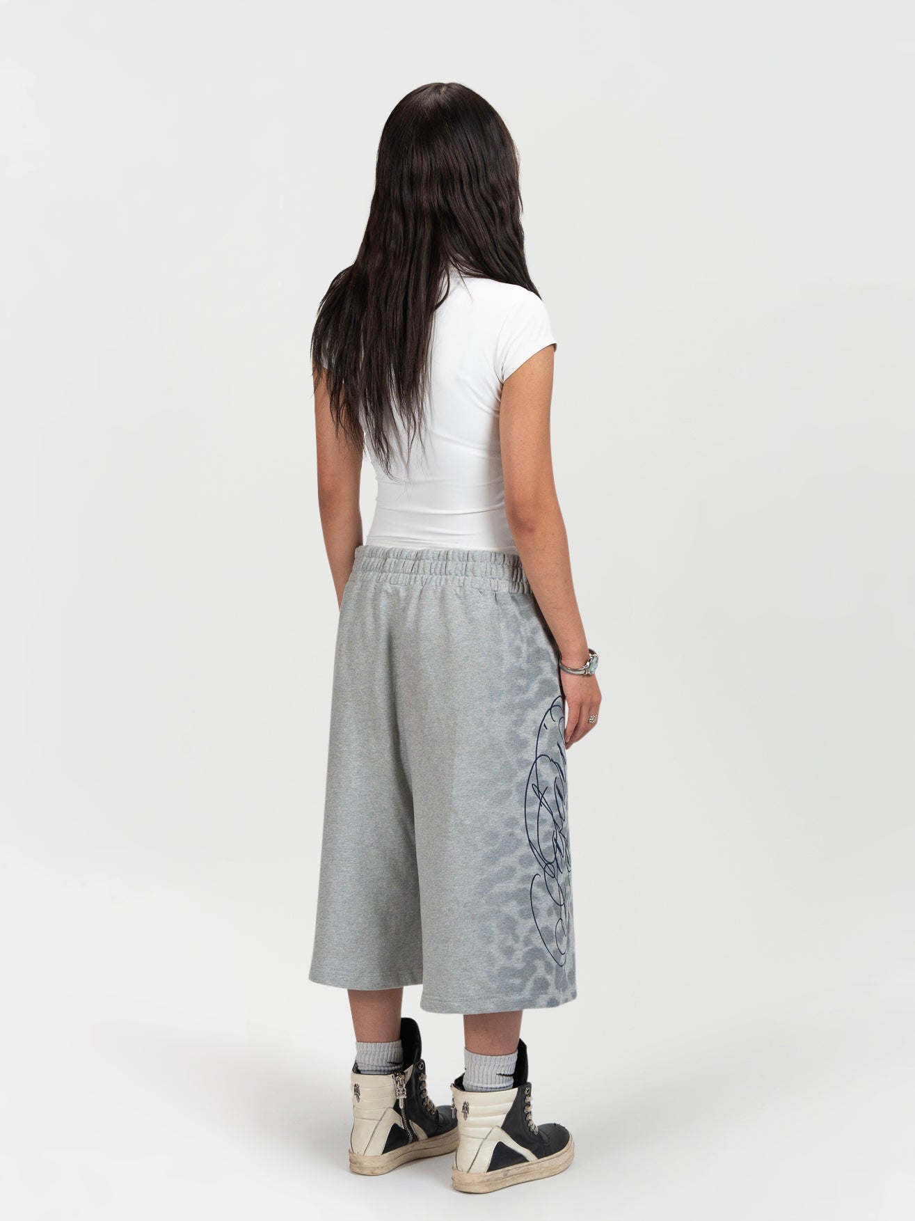 Back facing 45 degree full body shot of a female model wearing the jafari shrorts by J3T. she has on a cropped white t shirt, and black boots to complete the fit.