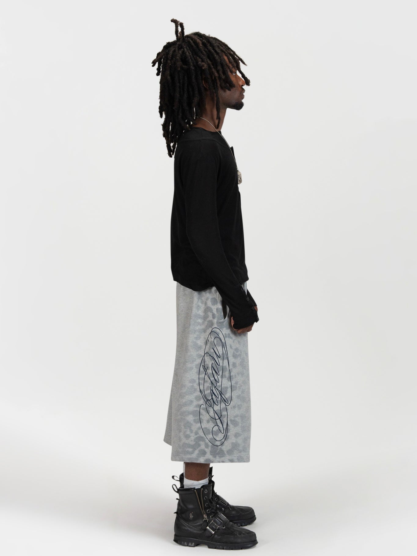 Side facing full body shot of a male model wearing the jafari shrorts by J3T. HE has on a black, long sleeve knit top , and black boots to complete the fit.