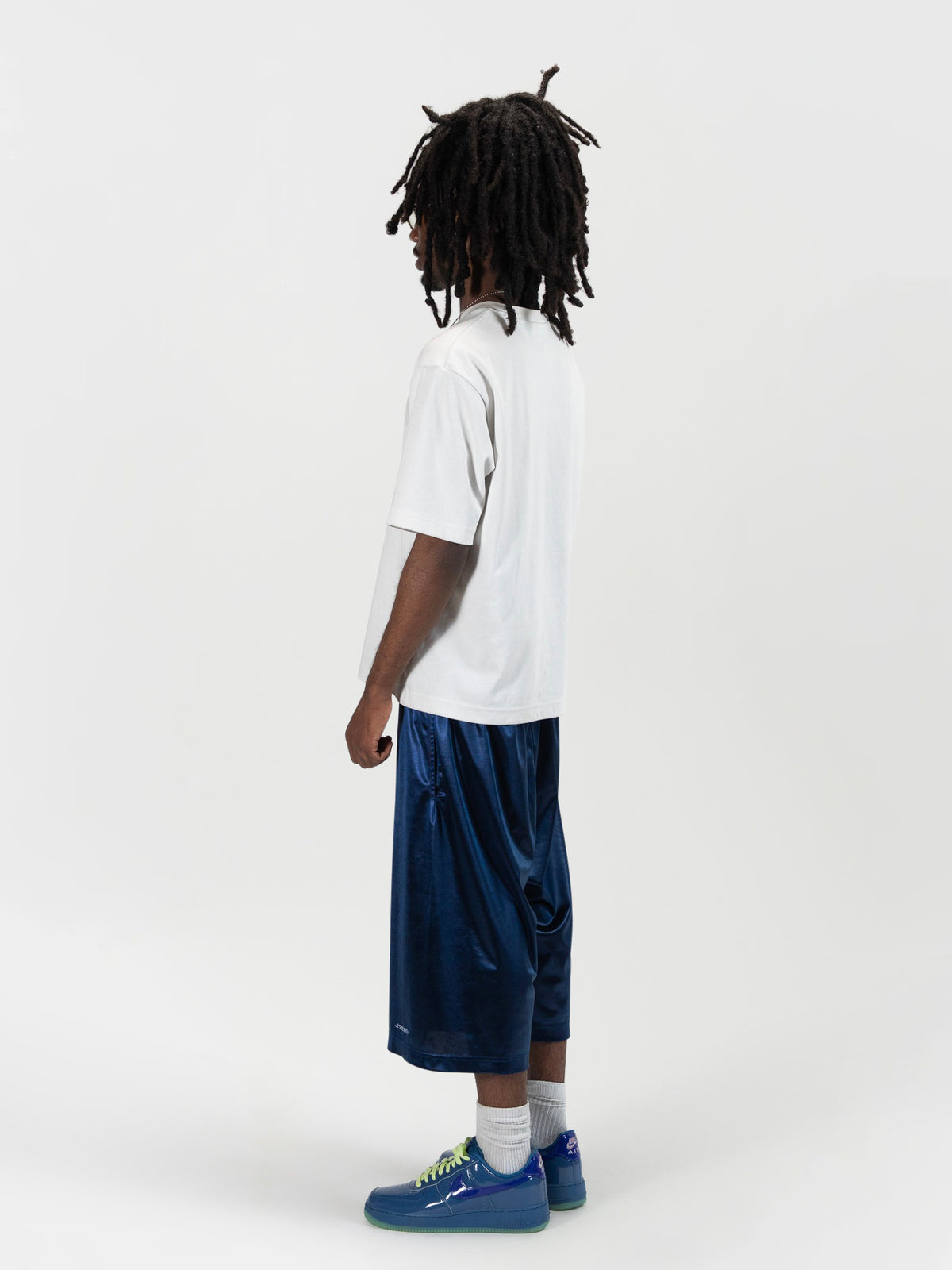 Back side 45 degree facing full body shot of a male model wearing the Tyson shrorts by J3T. HE has on a white shirt , and blue and yellow sneakers to complete the fit.
