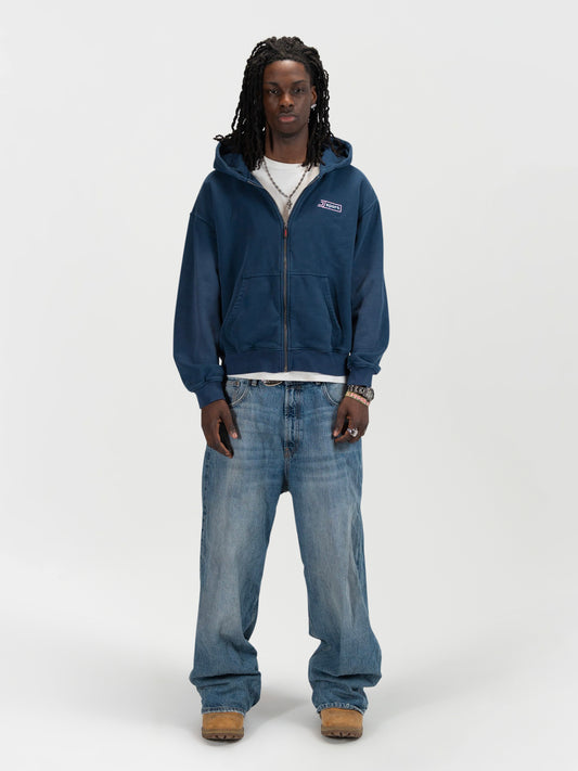Front facing full body shot of a male model wearing the J Sport zip by J3T. HE has on a white shirt underneath, light blue jeans and light brown boots to complete the fit.