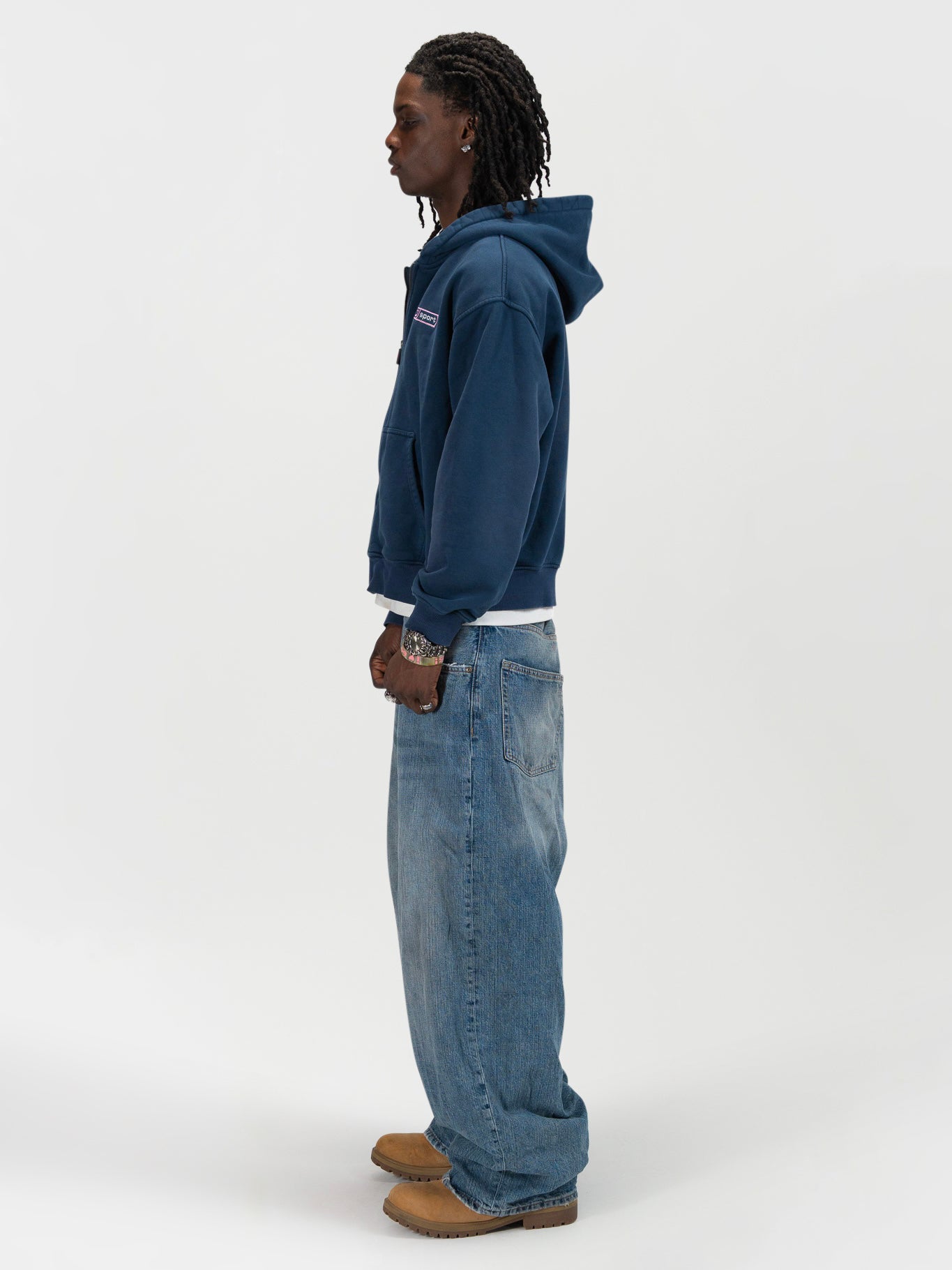 side facing full body shot of a male model wearing the J Sport zip by J3T. HE has on a white shirt underneath, light blue jeans and light brown boots to complete the fit.
