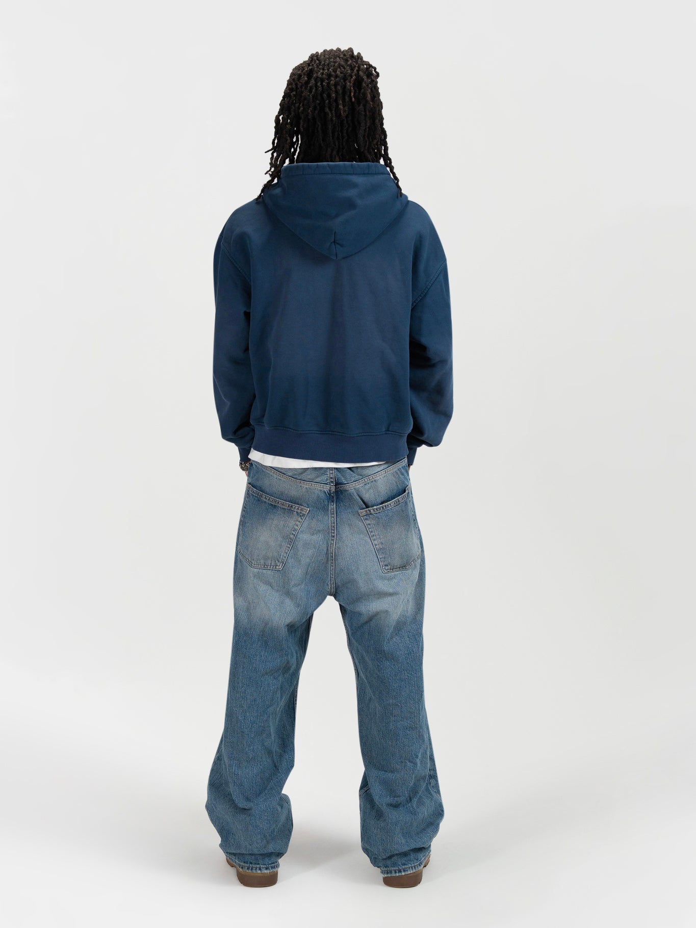 back facing full body shot of a male model wearing the J Sport zip by J3T. HE has on a white shirt underneath, light blue jeans and light brown boots to complete the fit.