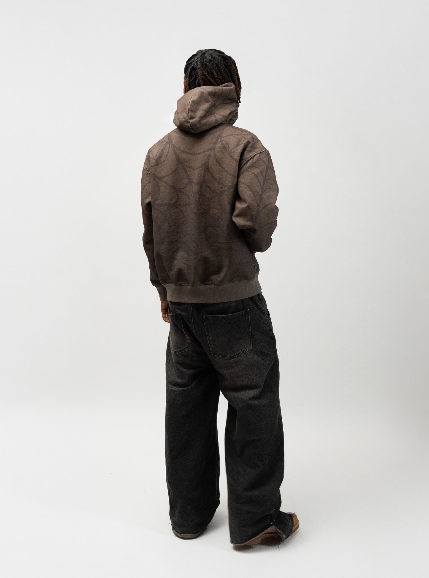 Full body angle of the model posing. He is turned away from the camera and facing the wall. he does not have the hood on and has his right hand in the pocket of the hoodie. J3T hoodie